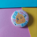 A round pin-back button badge featuring a cute cartoon chick character with the word 'FIX ON' and musical notes, displayed on a background of colorful paper blocks.