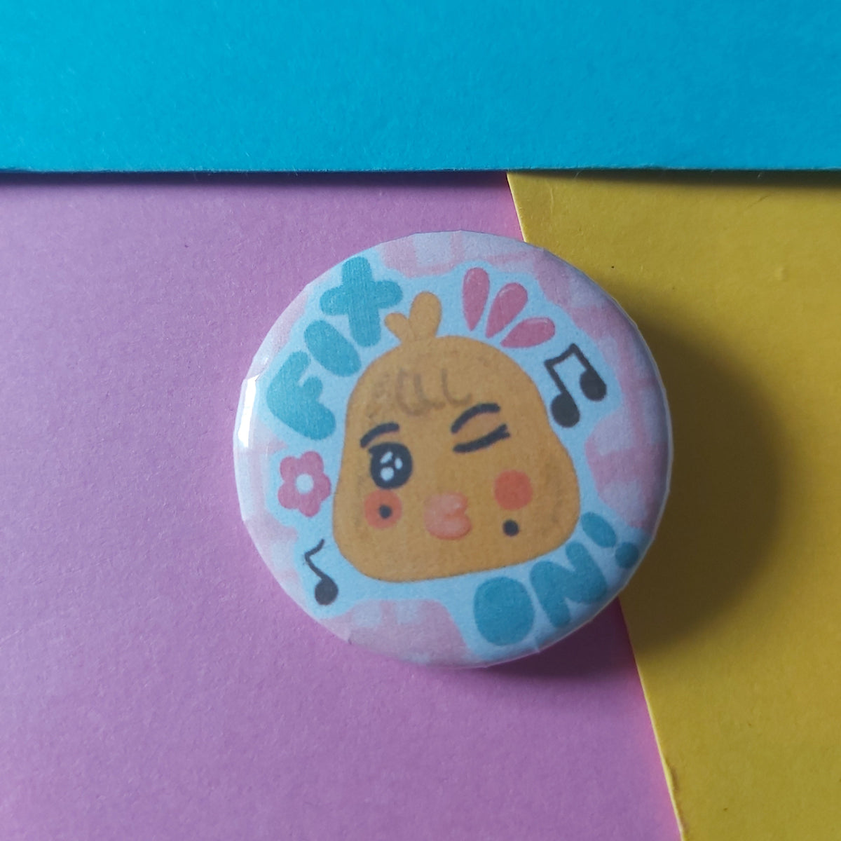 A round pinback button badge featuring a cute cartoon chick character winking, surrounded by musical notes, set against a background of split yellow and purple paper.