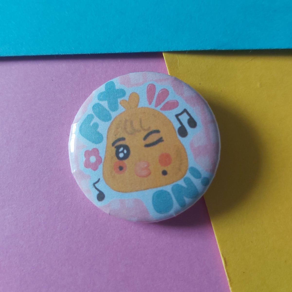 A round pinback button badge featuring a cute cartoon chick character winking, set against a background split diagonally into yellow and purple sections.