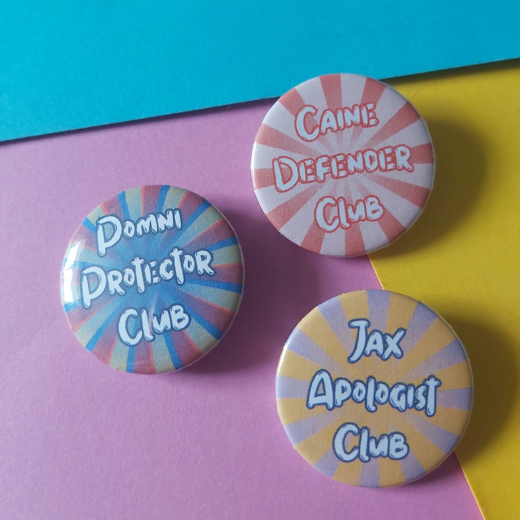 Three round pin-back buttons with colourful sunburst designs and text reading 'Caine Defender Club,' 'Jax Apologist Club,' and 'Pomni Protector Club,' arranged on a bright multicolour paper background.