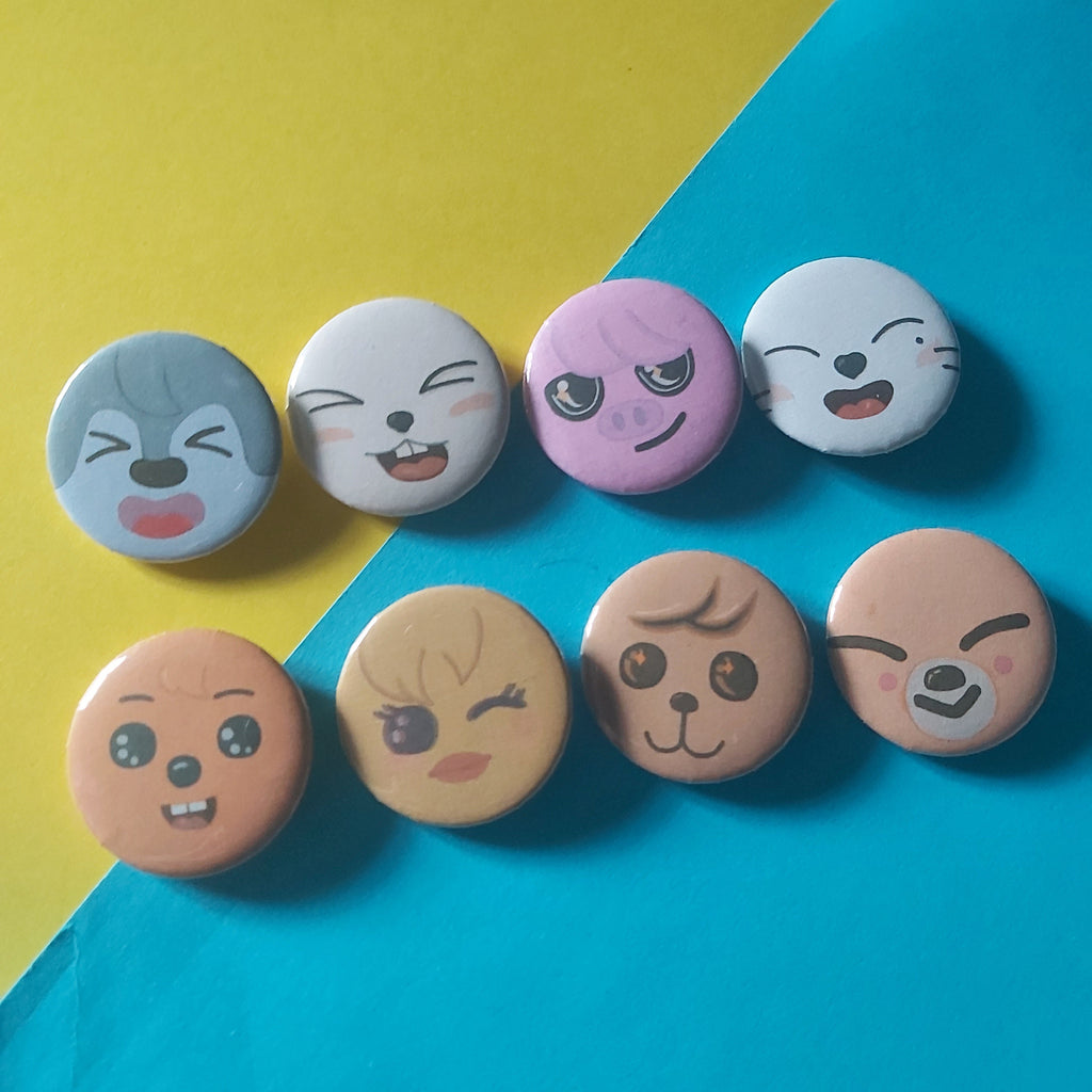 Eight small round pin-back buttons with cartoon face designs arranged in two vertical columns on a diagonally split yellow and bright blue background.