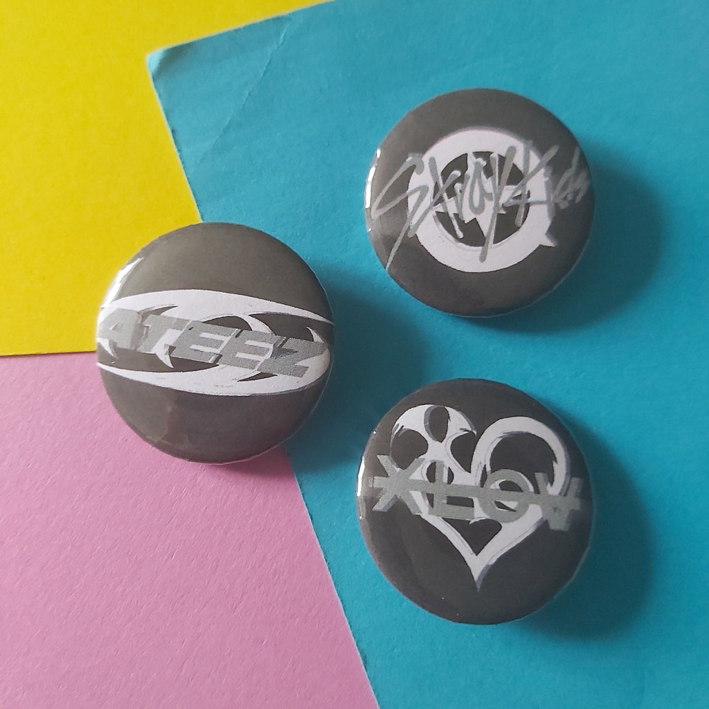 Three round gray button badges with stylized white graphic logos, arranged on a colorful background split diagonally between yellow, blue, and pink paper.