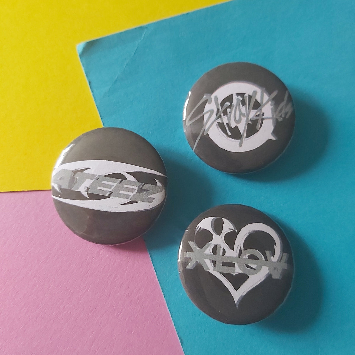Three round gray button badges with white stylized lettering, arranged on a colorful background split diagonally into yellow, blue, and pink sections.
