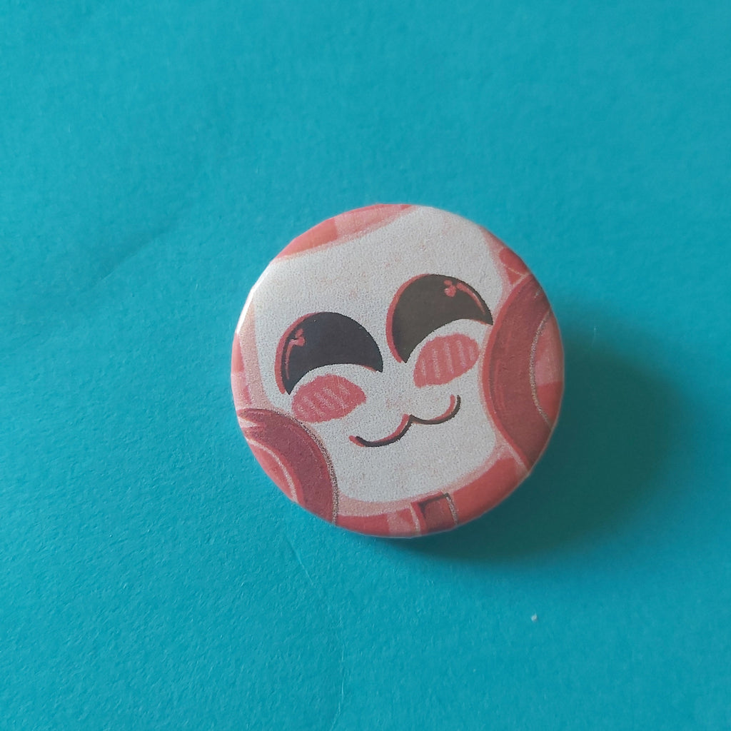 A round button badge featuring a stylised cutesy cartoon face with closed eyes on a white mask face and red ribbon hands, set against a solid teal-blue backdrop.