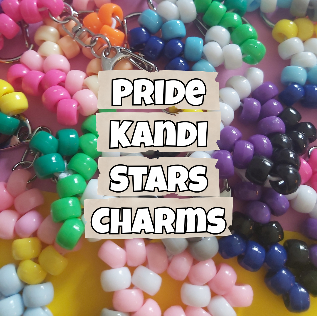 A close-up of multiple colorful beaded keychains arranged together, with a central paper label reading 'PRIDE KANDI STARS CHARMS'. The beads come in many bright colors including pink, green, blue, purple, white, yellow, orange, and black, attached to silver metal keyrings.