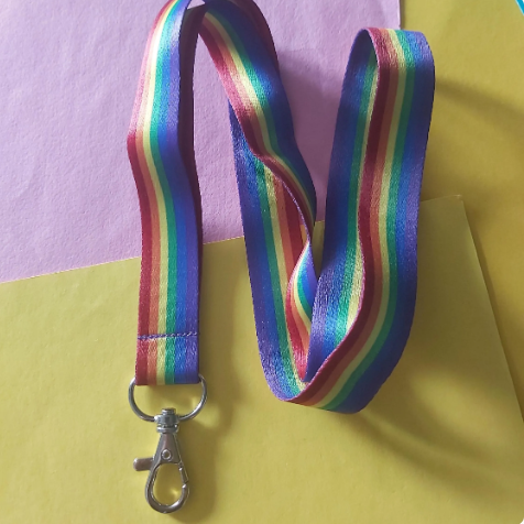 A rainbow-striped lanyard with a silver lobster clasp, laid out on a split yellow and purple background.
