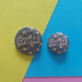 Two round button badges with a dark blue and yellow eye pattern and the word 'Cryptid' across the front
