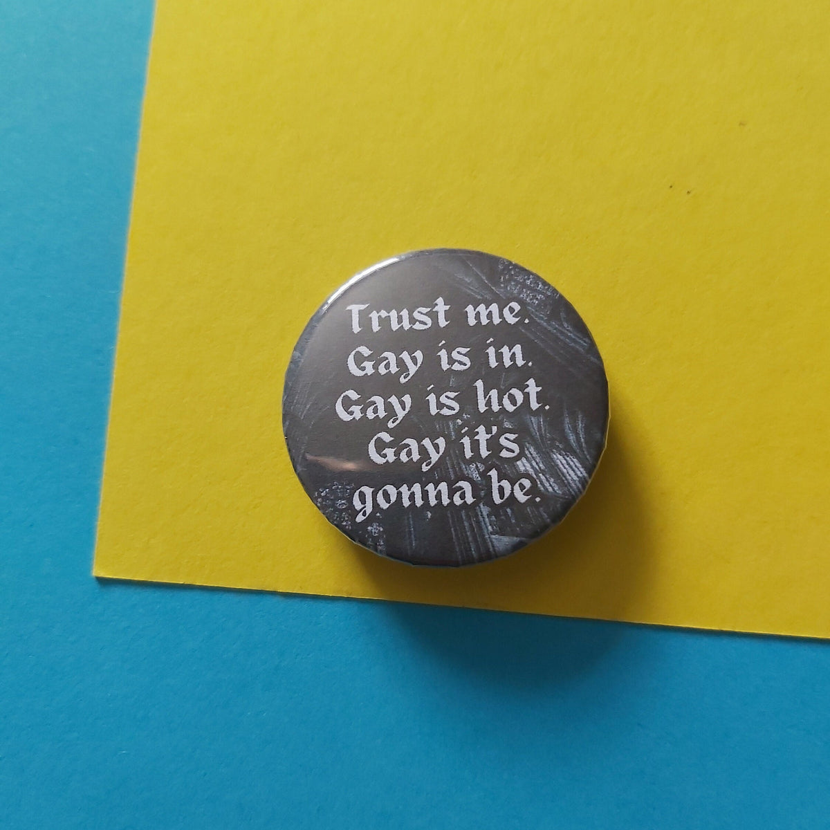 A round pinback button with the text 'Trust me. Gay is in. Gay is hot. Gay it's gonna be.
