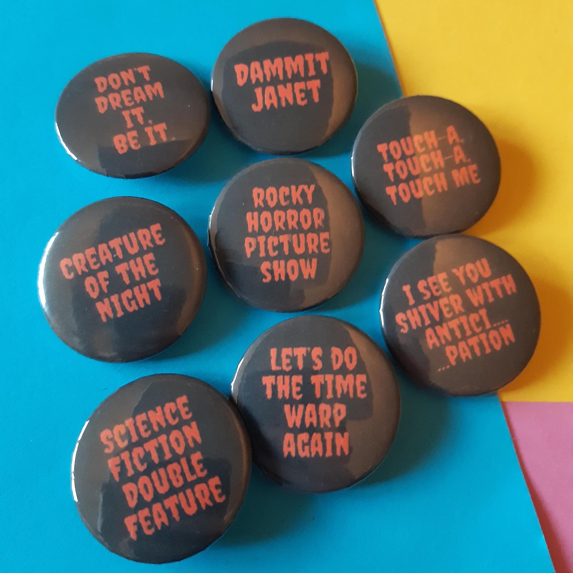 Seven round black pin-back buttons with pink text displaying quotes from The Rocky Horror Picture Show, arranged on a colourful background split diagonally between blue and yellow.
