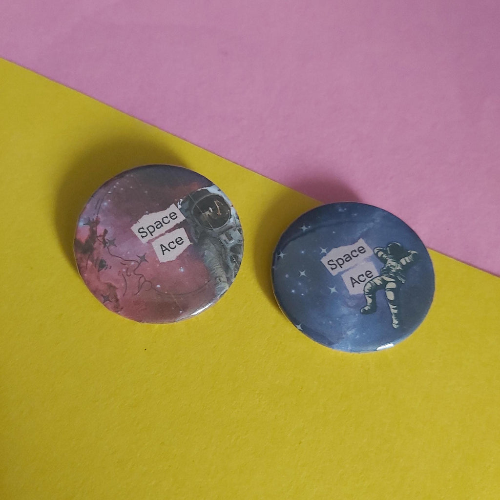 Two round pinback buttons with space-themed designs, one featuring a pink galaxy background and the other a purplegalaxy background, both with a white label reading 'Space Ace', displayed on a yellow and pink background.