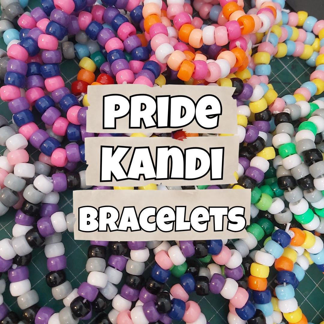 A pile of colourful beaded bracelets spread across a green cutting mat, with a central text overlay reading 'PRIDE KANDI BRACELETS'. The bracelets feature multiple colours, including pink, purple, blue, orange, yellow, green, black, and white.
