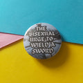 A round pinback button featuring the text 'THE BISEXUAL URGE, TO WIELD A SWORD' in white lettering over a dark fantasy scene