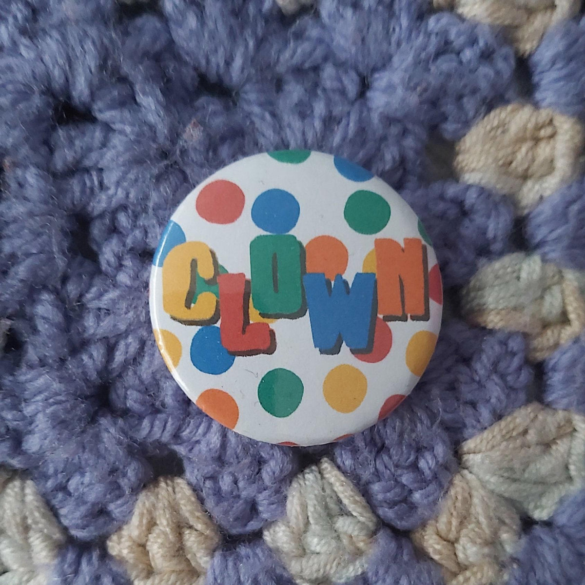 A round pinback button badge featuring the word 'CLOWN' in colourful block letters on a white background with multicoloured polka dots,