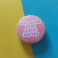 A round pink pinback button with the text 'Hot Girls Love Queer Horror' in white gothic lettering, set against a diagonally split yellow and blue background.