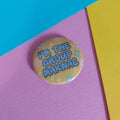 A round pinback button badge with the text 'I'M THE GROUP MAKNAE' in blue letters on a yellow background with small white and blue star patterns, resting on a pink surface with diagonal blue and yellow paper borders.