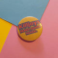 A round yellow pinback button with the text 'Killjoys Make some noise.' in red and blue, placed on a colorful background of pink, blue, and yellow paper.