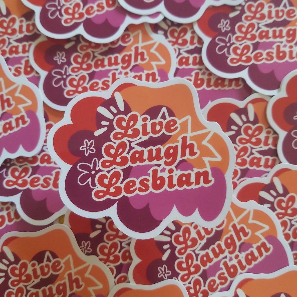 A close-up pile of die-cut stickers featuring the phrase 'Live Laugh Lesbian' in red script over a retro cloud and starburst design in orange, pink, and purple with white outlines.