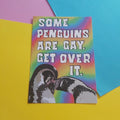 A rectangular print with a rainbow gradient background and bold white text reading “SOME PENGUINS ARE GAY.  GET OVER IT. And a penguin couple in the lower left corner