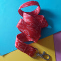A red fabric lanyard strap with a white line-art pattern of teeth, attached to a silver metal lobster clasp, arranged on a colorful background of blue, yellow, and purple paper.