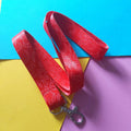 A red fabric lanyard with a repeating white line-art pattern and a silver metal lobster clasp, laid flat on a colourful background of blue, yellow, and purple paper.