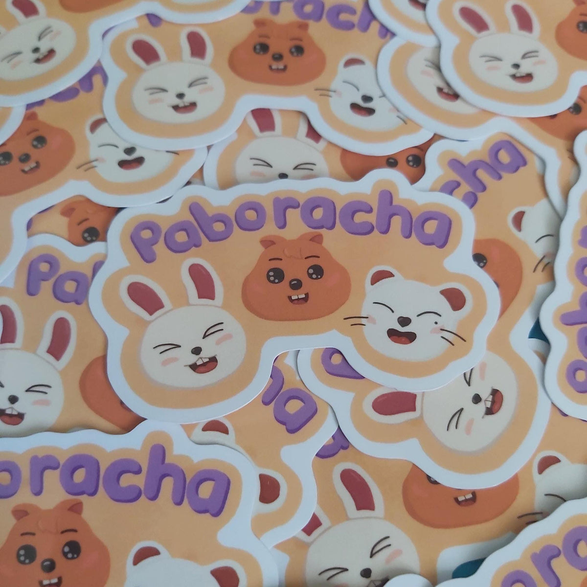 A pile of cute cartoon stickers featuring the word 'Paboracha' in purple lettering, with white bunny and ferret faces, brown quokka illustrations, and pink accents on a peach background.