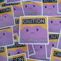 A pile of die-cut stickers featuring a cartoon purple blob face with black eyes and a smile, set against a yellow background with a black banner reading 'CAUTION DITTO AT WORK'.