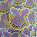A close-up of multiple die-cut stickers featuring a purple cartoon bunny face with the text 'I DON'T care' on a yellow and blue geometric background.