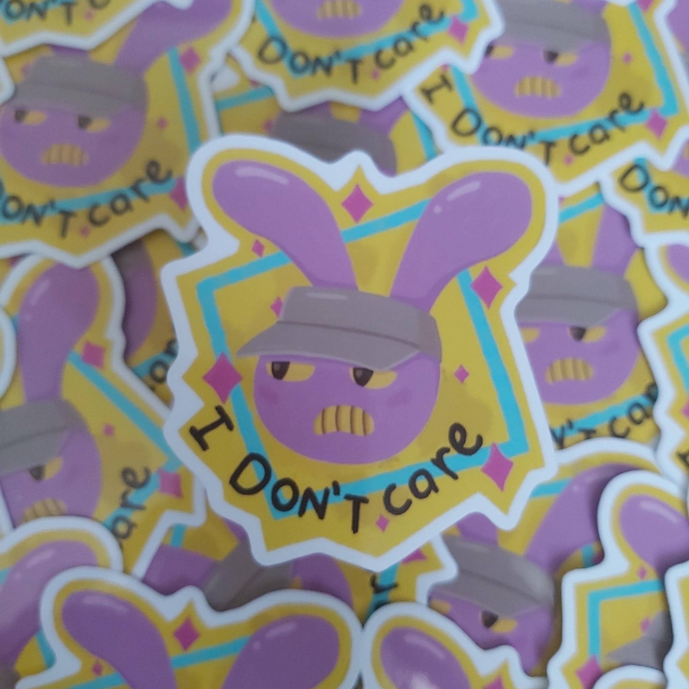 A close-up of multiple die-cut stickers featuring a purple cartoon bunny face with the text 'I DON'T care' on a yellow and blue geometric background.