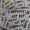 A pile of white die-cut stickers featuring the text 'VAMPIRES ARE GAY' in a black hand-drawn font, accompanied by black line drawings of vampire teeth. 