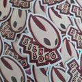 A pile of die-cut stickers featuring a character with a cream face and dark eyes, with the text 'SILK SONG' on a jagged banner. The stickers are shown overlapping on a burgundy background.