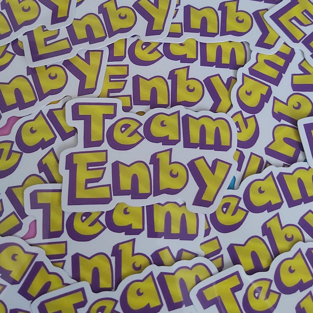 A pile of die-cut stickers featuring the text 'Team Enbya' in bold yellow letters with a purple outline on a white background.