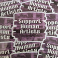 A close-up of multiple die-cut stickers with the phrase 'Support Human Artists' in white text over a textured purple and black background, arranged with overlapping matching stickers.