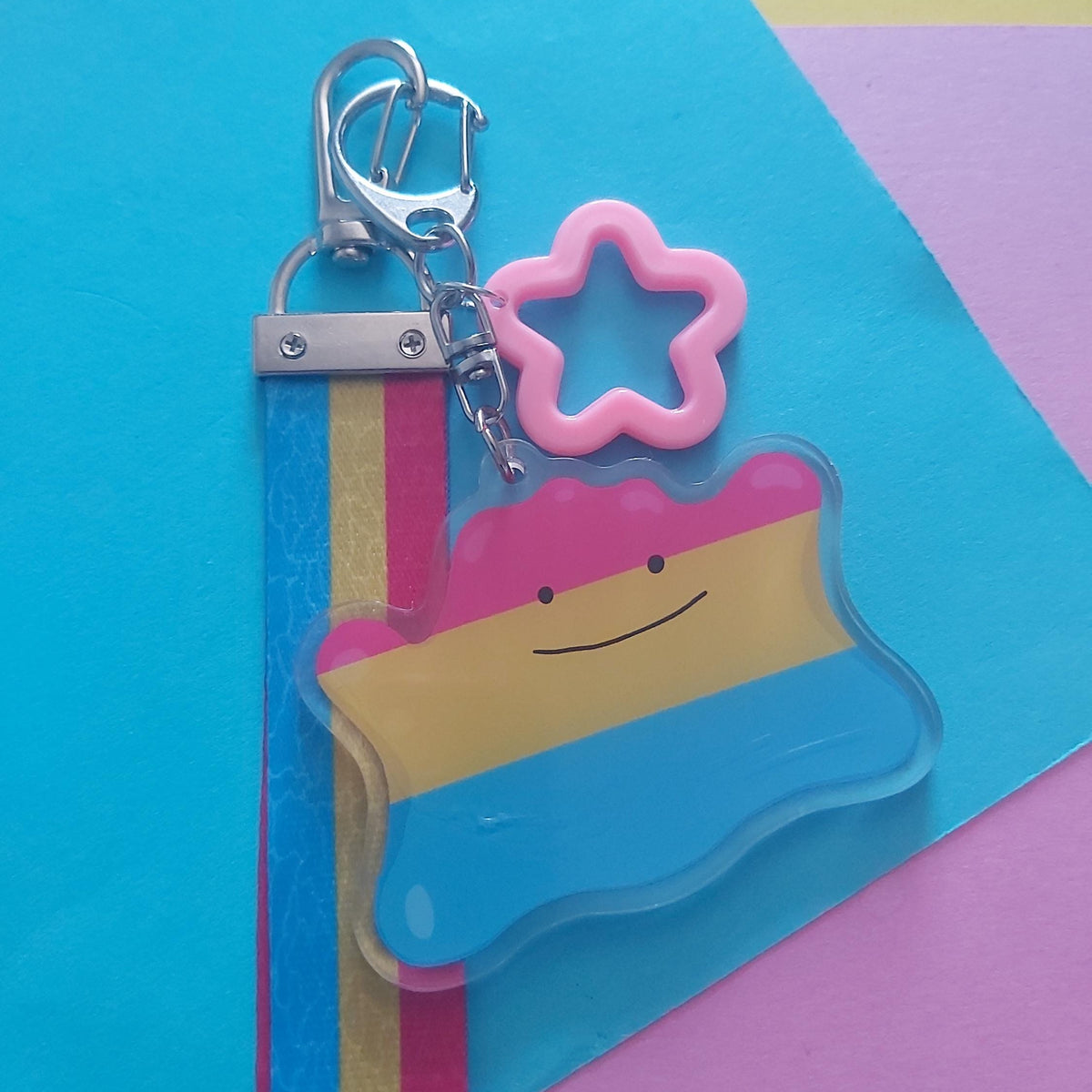 A striped keychain charm with a pink star-shaped ring and silver clasp, photographed on a colourful geometric paper background.