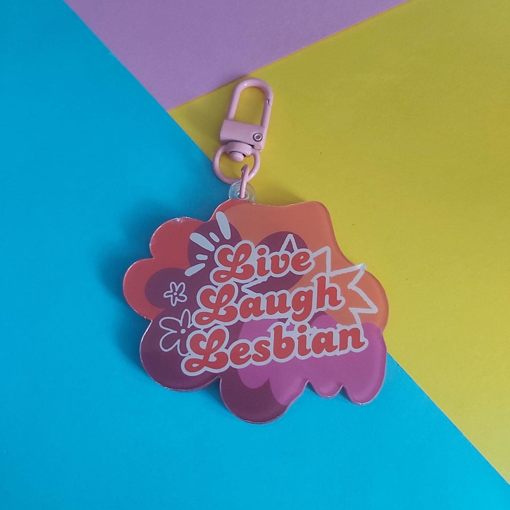 An acrylic keychain with the text 'Live Laugh Lesbian' in pink script, set against a background of diagonal colour blocks in cyan, yellow, and pink.