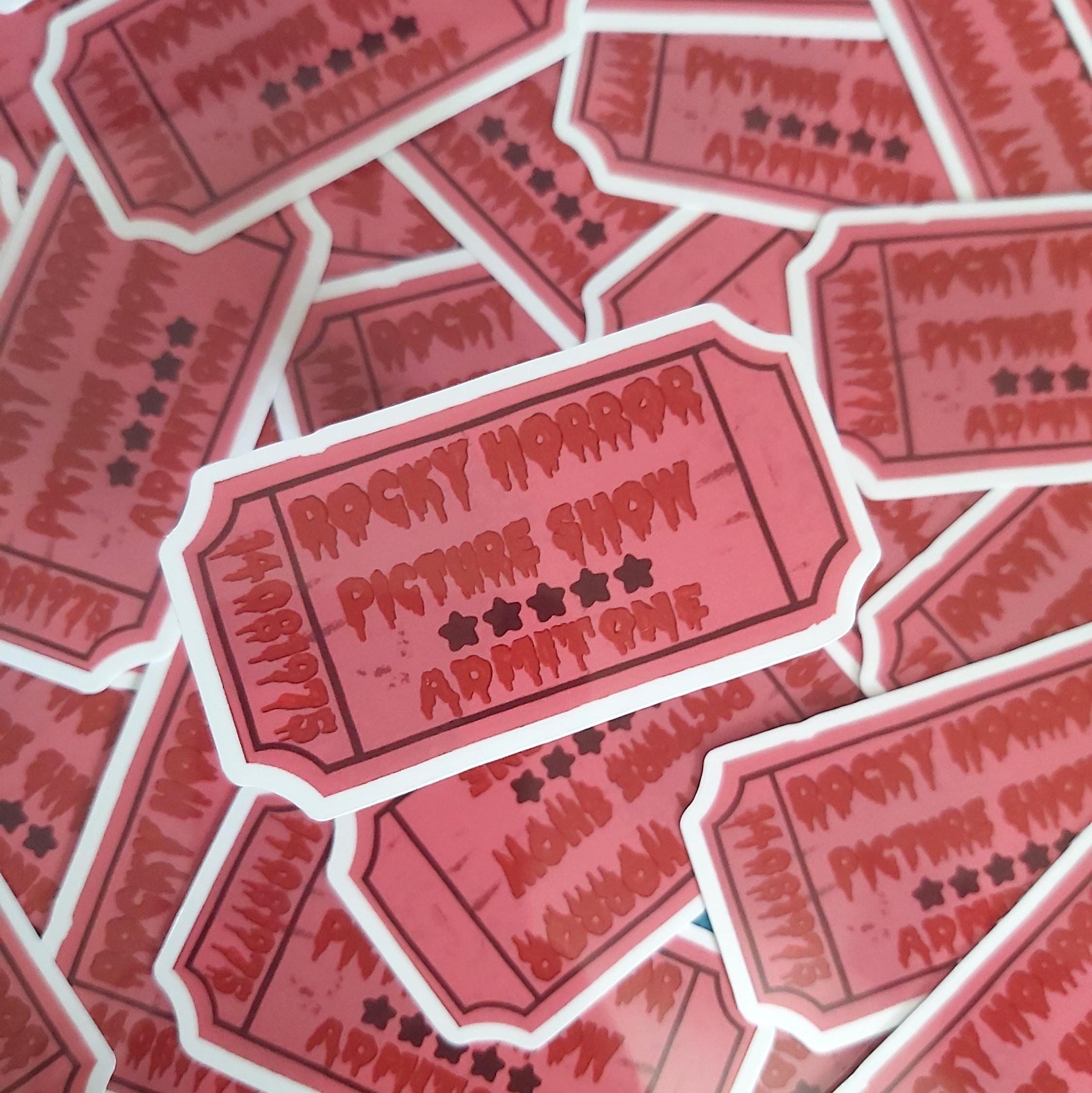 A pile of die-cut stickers shaped like vintage movie tickets, featuring the text 'ROCKY HORROR PICTURE SHOW ADMIT ONE' in a distressed red font on a pink background with white borders.