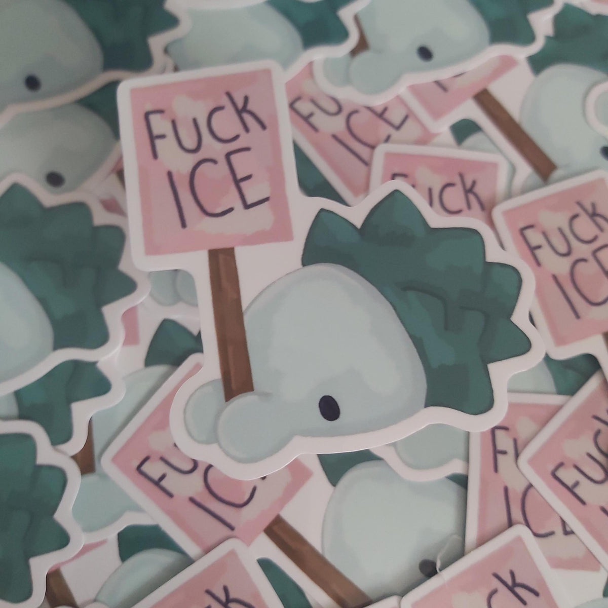 A pile of die-cut stickers featuring a Pokémon called Snom holding a sign that reads 'FUCK ICE' in black handwritten-style lettering. The stickers have a white border and are shown overlapping in a close-up shot.