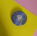A round pin badge featuring a space-themed design with a purple starry galaxy background and an astronaut graphic that reads 'Space Ace'. The badge is placed on a split yellow and pink background.