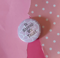A round pinback button badge with the text 'IN SAPPHO WE TRUST' in black lettering, set against a background of torn pink paper and pink polka-dot paper.
