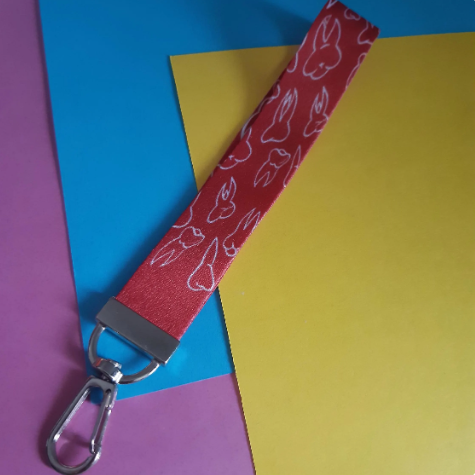 A red fabric wrist strap with a white teeth pattern and a silver metal clasp, laid diagonally over colourful paper sheets.